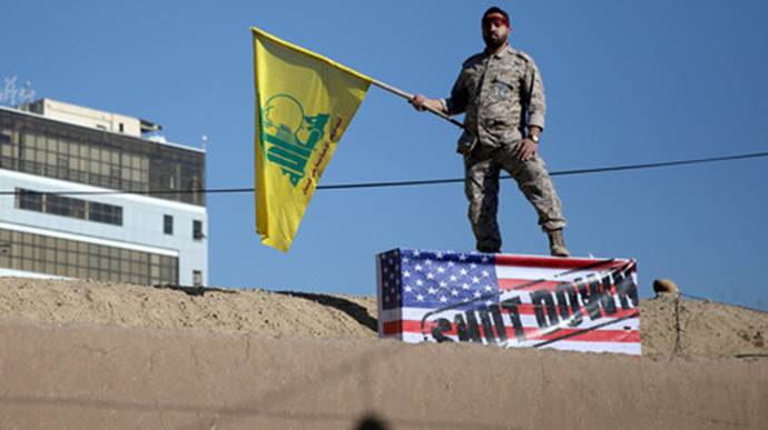 Eine iranische Wache hält eine Hisbollah-Flagge während des Trauerzuges bei der Beerdigung von Soleimani in Kerman und steht dabei auf einer US-Flagge. Auf dieser steht: 
